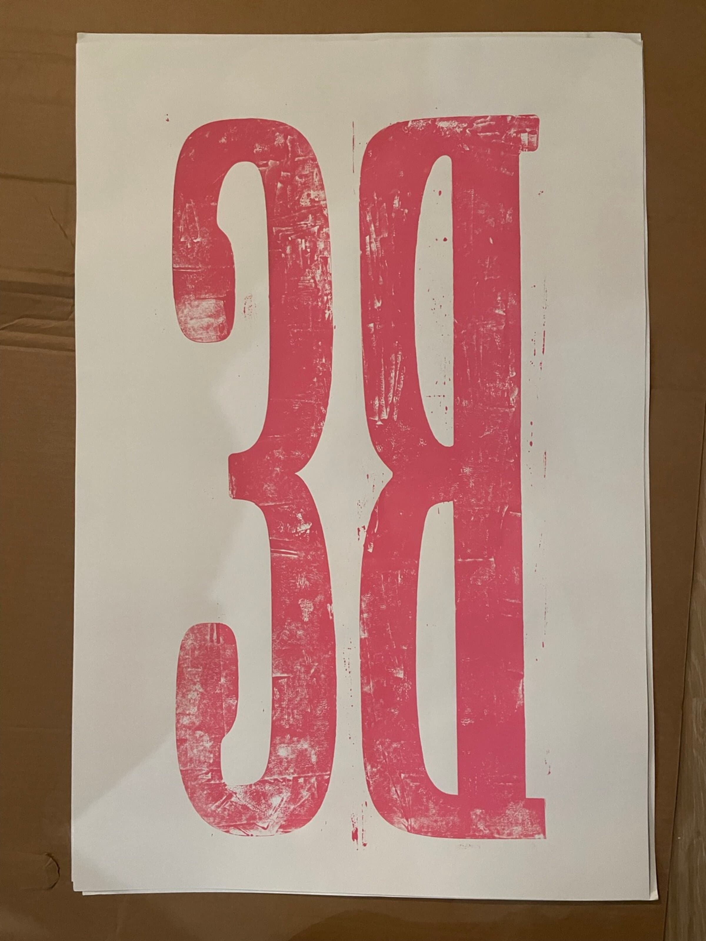 The full pull of the giant BS blocks on a single sheet of white paper laid on cardboard: massive hot-pink letterforms reading B over S stacked vertically across the sheet, the impression heavily distressed where the ink loaded unevenly across the broad inked surface, the carved counters of each letter punching through to the white.