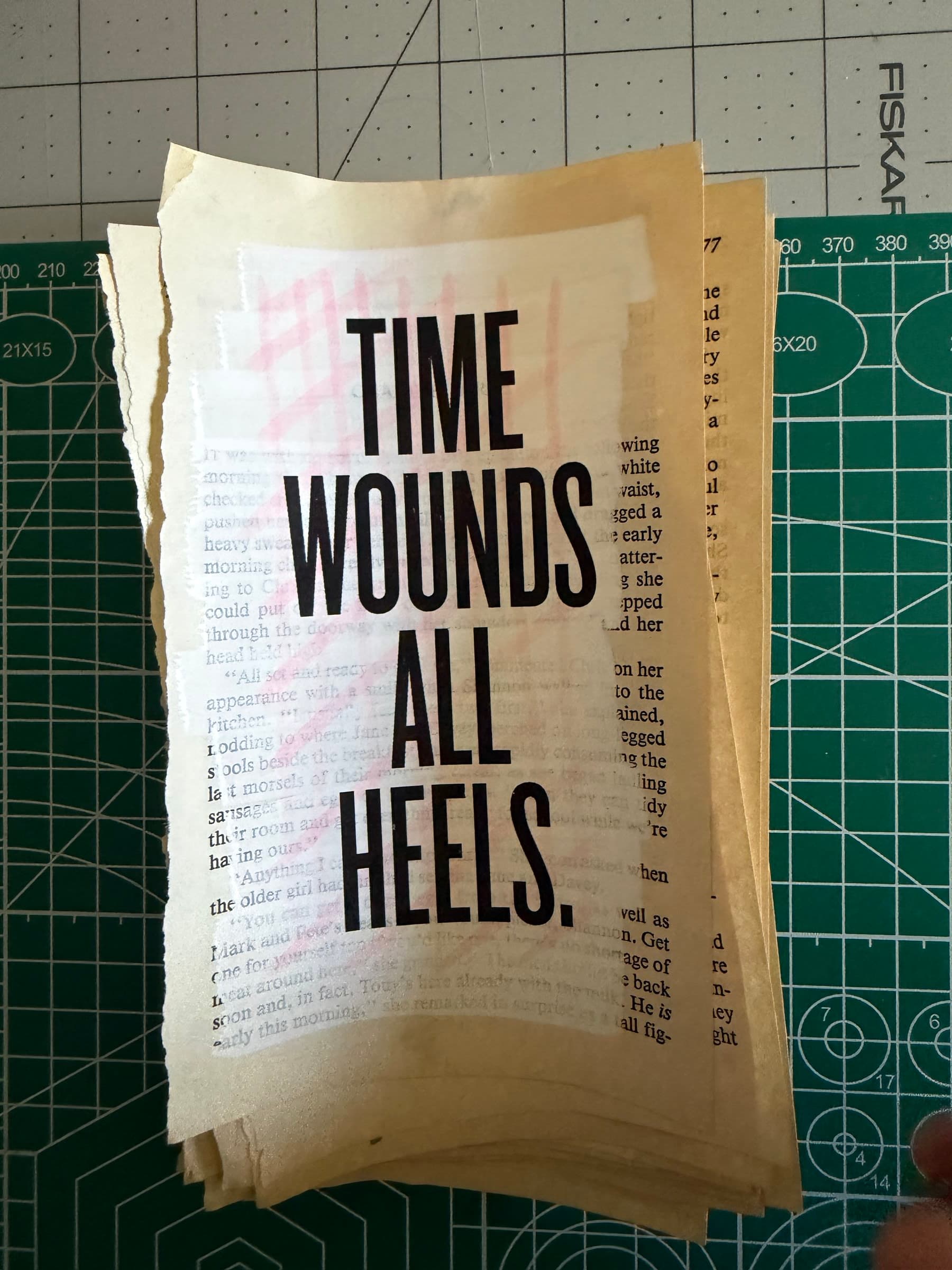A torn paperback page on a green cutting mat. Across the warm aged paper, a pale red watercolor wash runs as a horizontal color block. Overprinted in tall chunky display caps: TIME WOUNDS ALL HEELS. The original paperback prose runs underneath the color block, ghosted but legible.