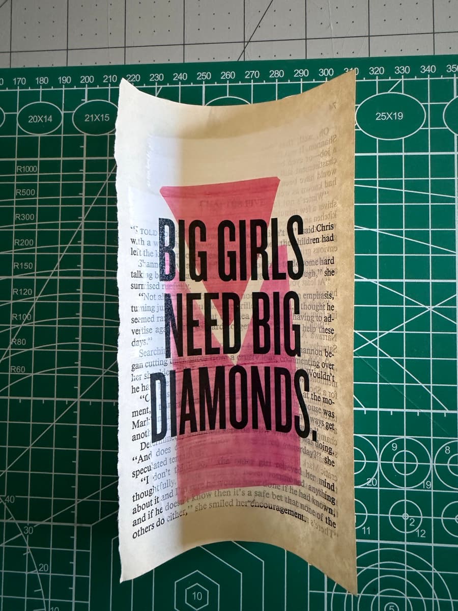 BIG GIRLS NEED BIG DIAMONDS : over a brick-red painted block on a torn paperback page