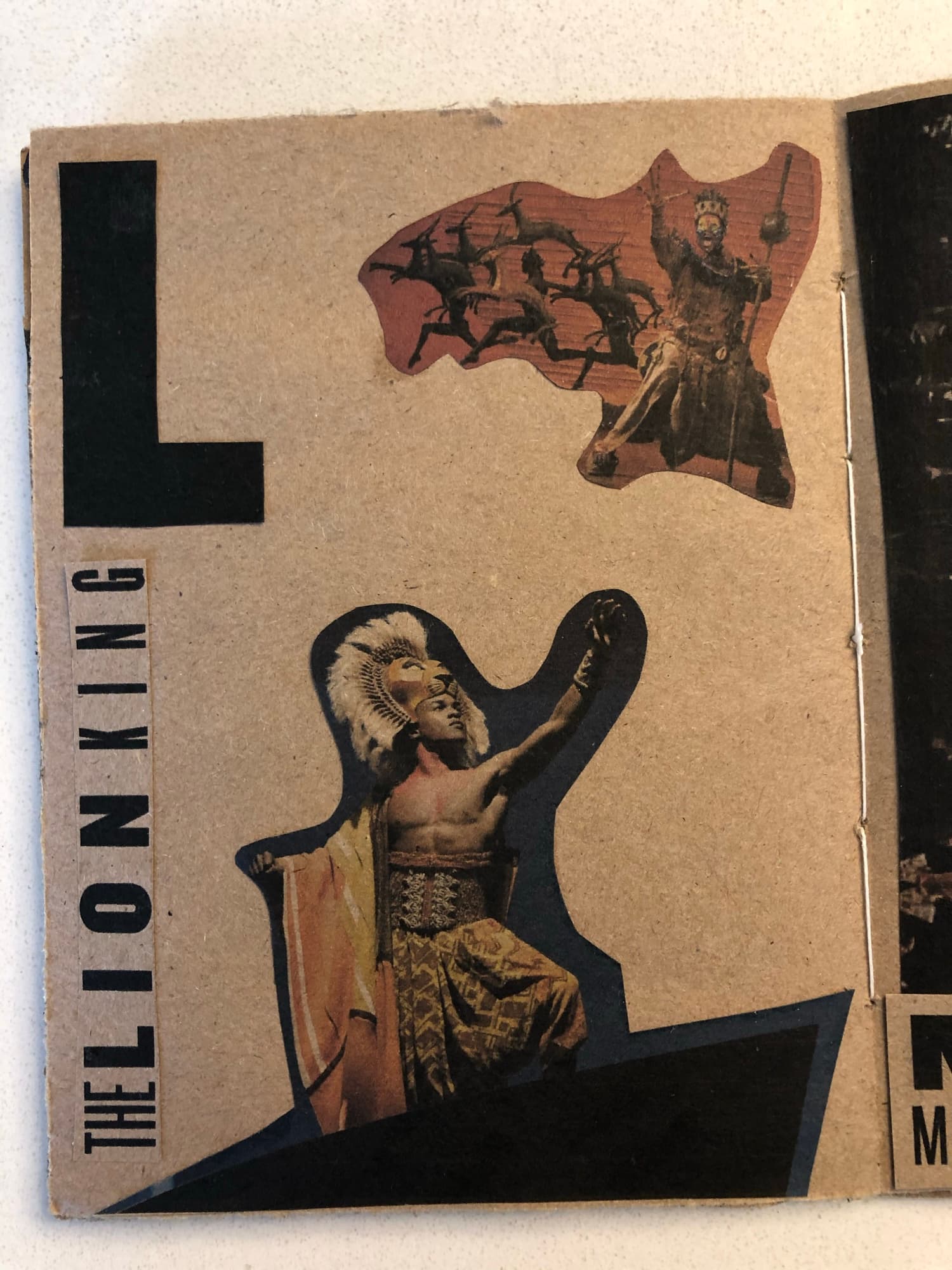L spread: silhouetted figures and torn paper assembled around a deep L, the words THE LION KING set inverted at the bottom of the page