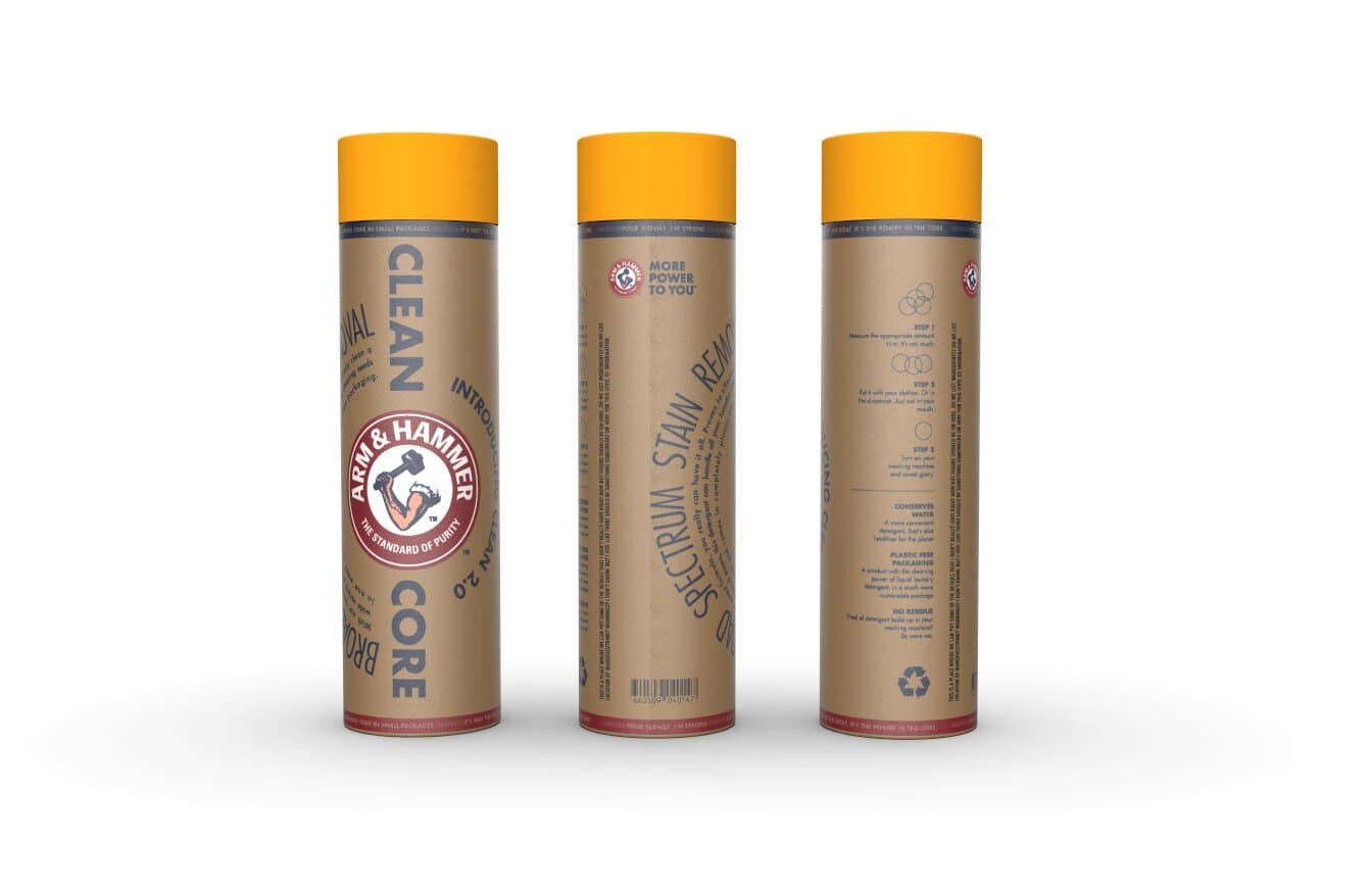 The Clean Core 2.0 final shipping package shown from three angles: a cylindrical kraft cardboard tube with a sunny yellow cap, the Arm & Hammer mark anchored centrally on the front panel, with CLEAN CORE set in vertical chunky display caps to the right of the mark and Spectrum Stain Removal copy rotating down the body. The back panel shows the same three-step instructions and a sustainability message.
