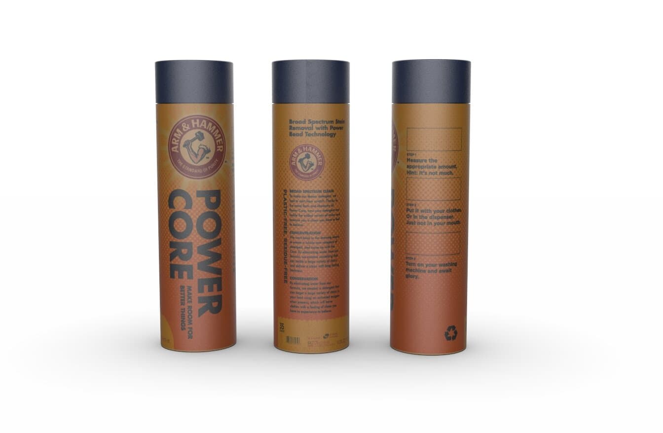 The Power Core final shipping package shown from three angles: a cylindrical kraft cardboard tube with a deep navy-charcoal cap, terracotta-orange body printed with the Arm & Hammer mark and POWER CORE set in chunky white display caps running vertically. The center angle shows the back panel with body copy under 'Broad Spectrum Stain Removal with Power Bead Technology.' The right-side angle shows the three-step instructions with simple line illustrations.