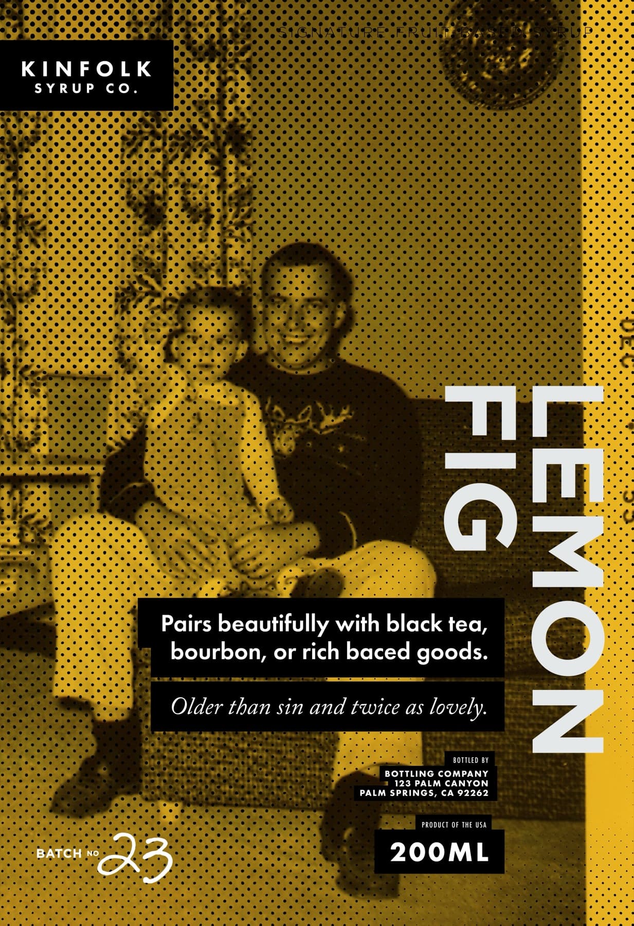 The original Lemon Fig poster: a vintage family photograph of a father holding a small child on his lap in an armchair, halftoned and washed in Kinfolk's warm gold, LEMON FIG set in tall white display caps down the right edge, the serving line 'Pairs beautifully with black tea, bourbon, or rich baked goods' and the personality line 'Older than sin and twice as lovely' set on black panels, BATCH NO 23 in handwritten script at the foot.