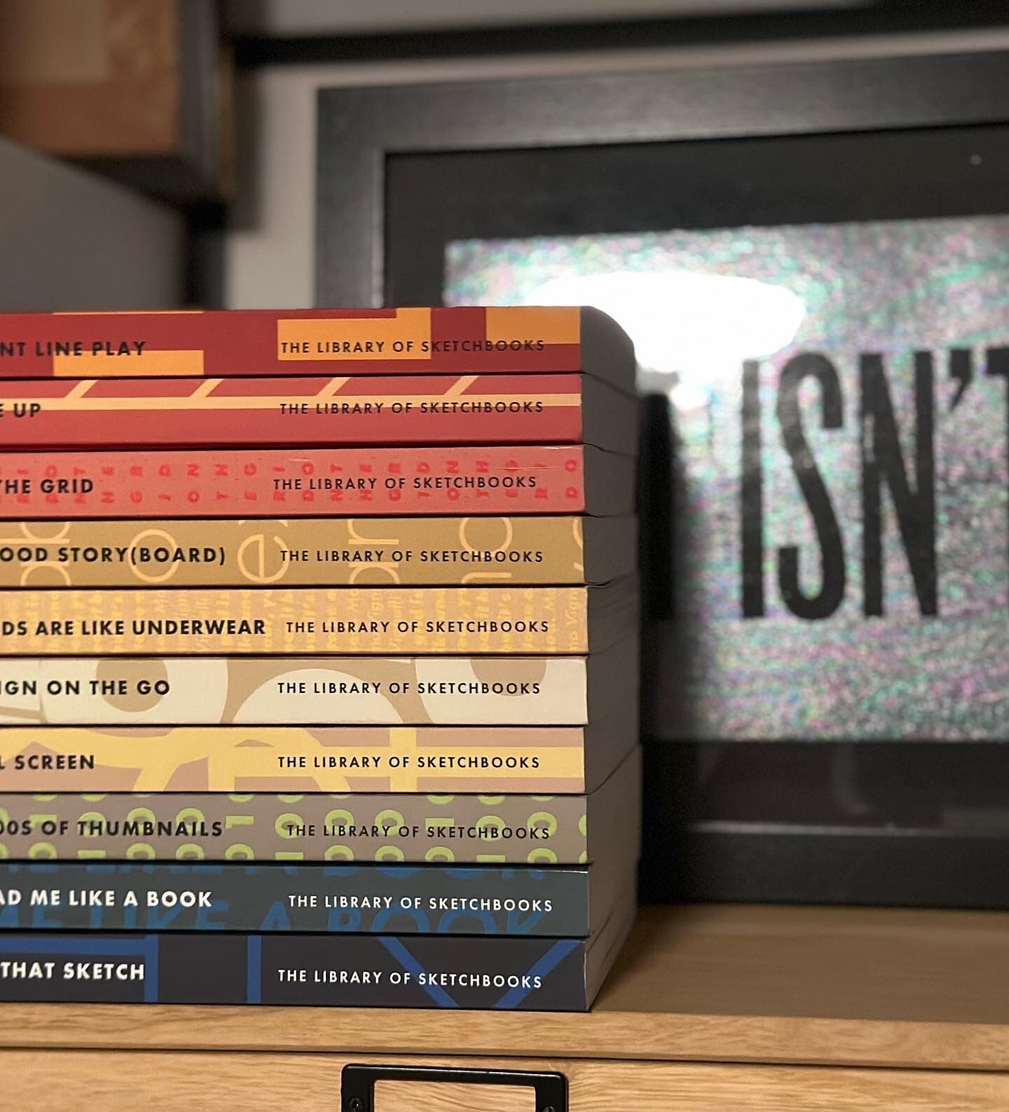 A stack of ten sketchbooks viewed from the side: each spine prints THE LIBRARY OF SKETCHBOOKS in matching display caps, with the individual title (POINT LINE PLAY, LINE UP, ON THE GRID, A GOOD STORY(BOARD), GRIDS ARE LIKE UNDERWEAR, DESIGN ON THE GO, FULL SCREEN, 1000s OF THUMBNAILS, READ ME LIKE A BOOK, ALL THAT SKETCH) tucked next to it. Each cover is its own color and pattern, so the stack looks like a small shelf of Penguin classics for designers.