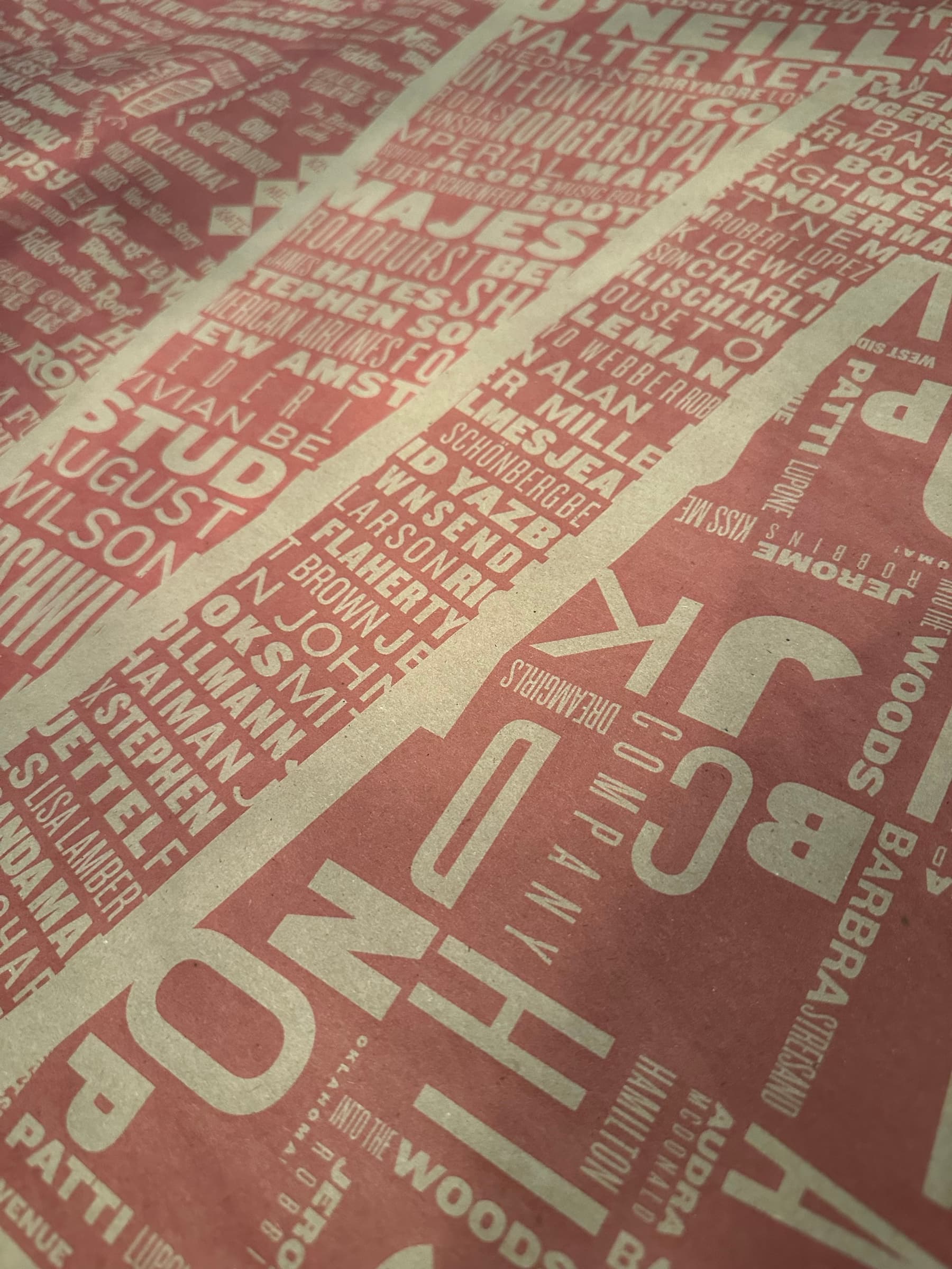 An intimate close-up of the alphabet paper held in soft directional light: oversized letters BCJK, NOP, HI, AB visible in the foreground, and the smaller display type of Sondheim, Audra McDonald, Hamilton, Patti LuPone, Stephen, Lincoln Center reading underneath in cream.