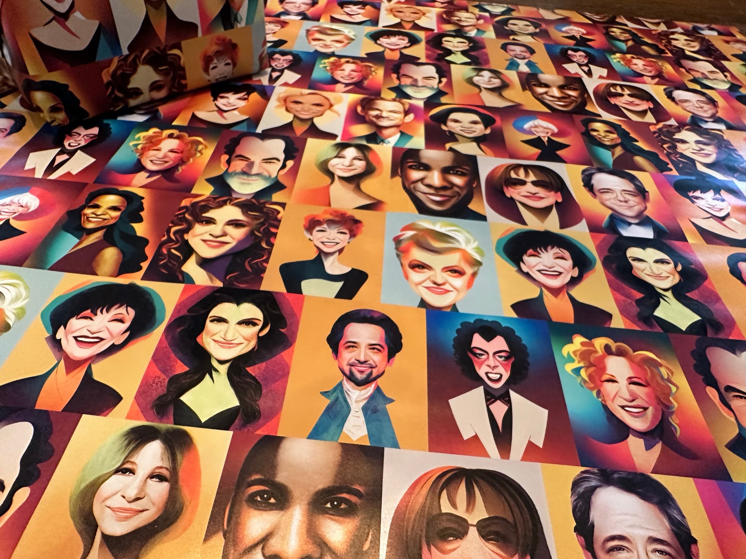 A perspective view of the portrait paper laid across a wood floor: the grid of caricatures (Lin-Manuel Miranda, Bernadette Peters, Idina Menzel, Liza Minnelli, Bette Midler, Carol Burnett, Audra McDonald, Whoopi Goldberg, and others) recedes into the depth of the frame, the tile rhythm carrying every direction.