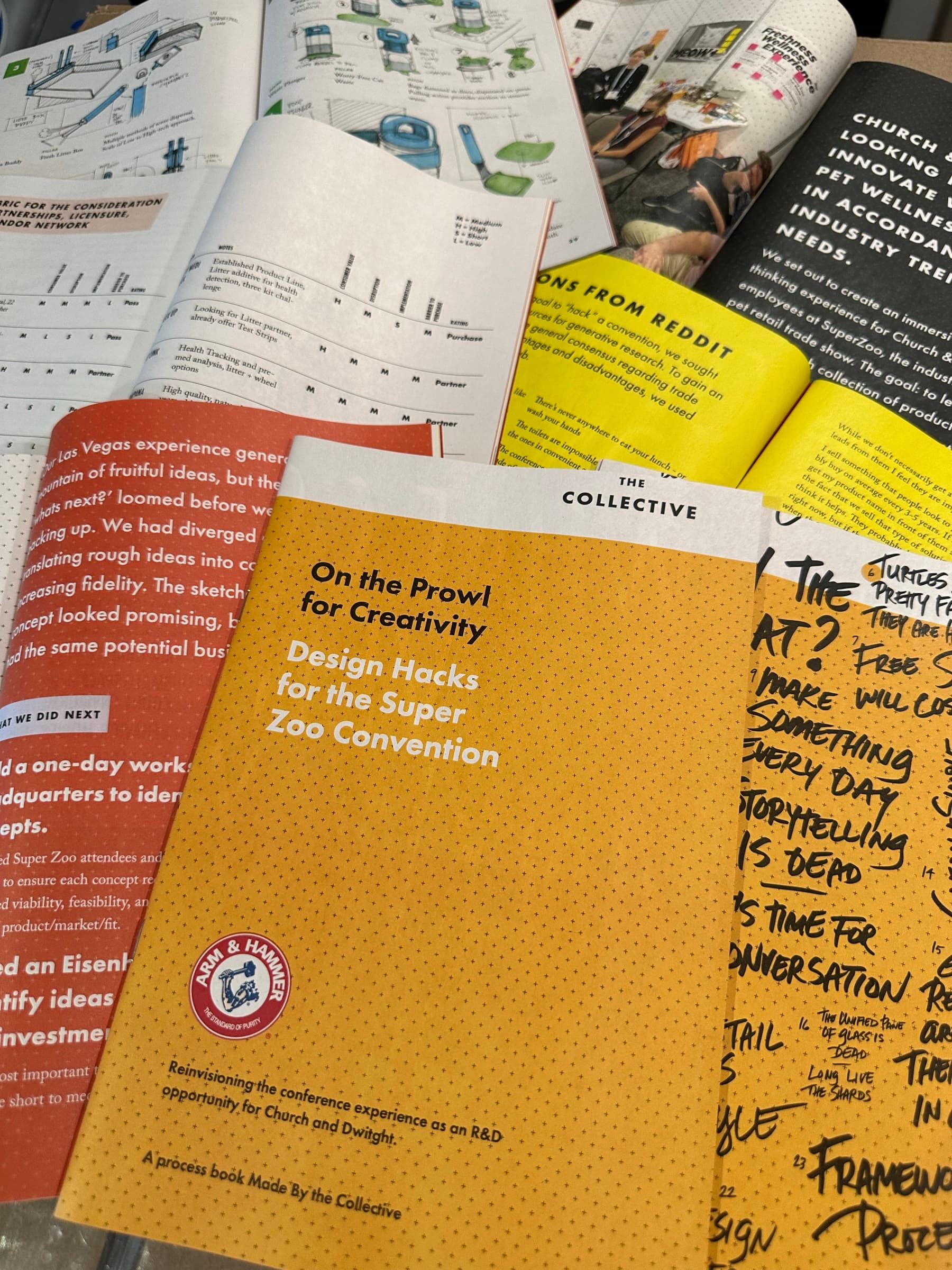 A flat lay on a desk: the printed ZooFari process book ('On the Prowl for Creativity / Design Hacks for the Super Zoo Convention') sits in the center next to a yellow handwritten brainstorming page filled with provocations like 'What if storytelling is dead?' and 'Make something every day,' a printed bar-chart research insert, a 'How might we' worksheet, and a row of How-Might-We frameworks lined up across the bottom.
