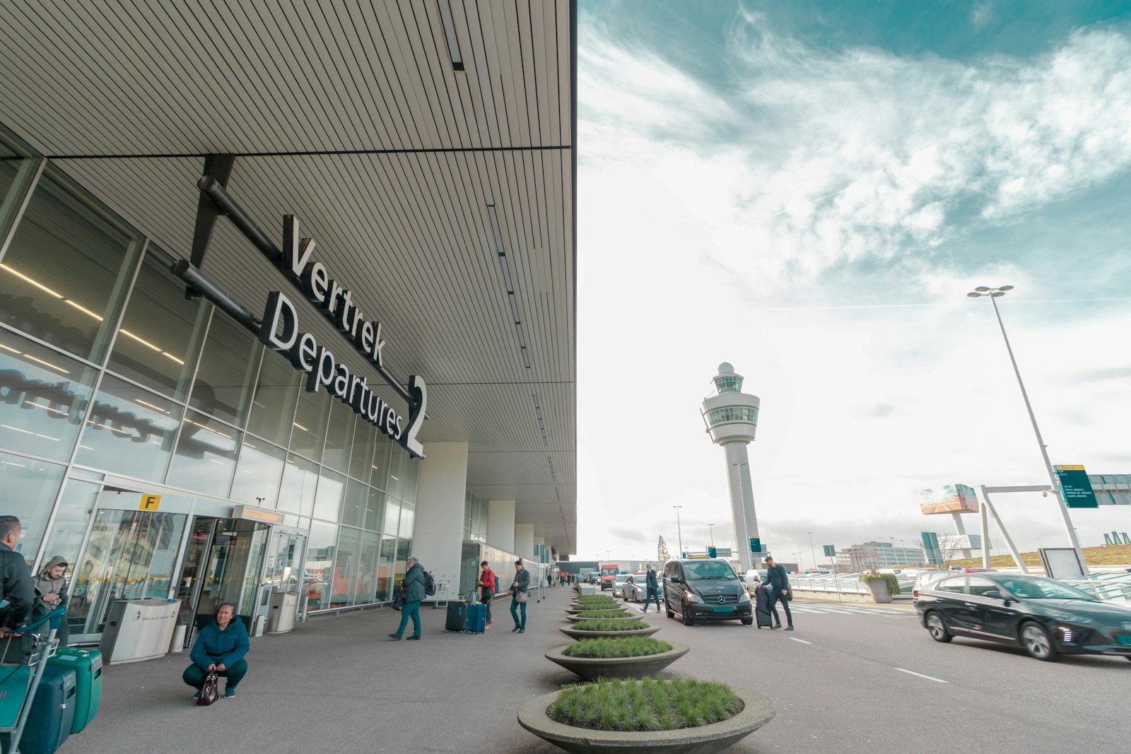 Schiphol Airport Departures 2 entrance: yellow wayfinding sign reading 'Vertrek Departures 2' with the control tower visible behind